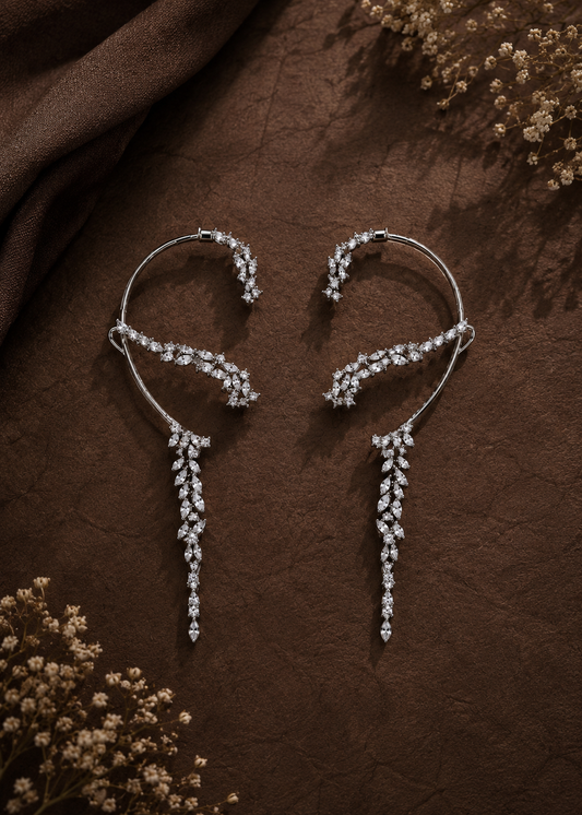 Silver statement ear cuffs with cascading crystal leaves displayed on a brown textured background.