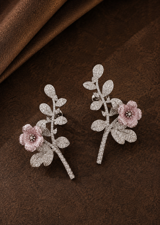 Silver statement floral ear cuffs featuring pink enamel blossom and crystal leaf detailing on brown textured background.