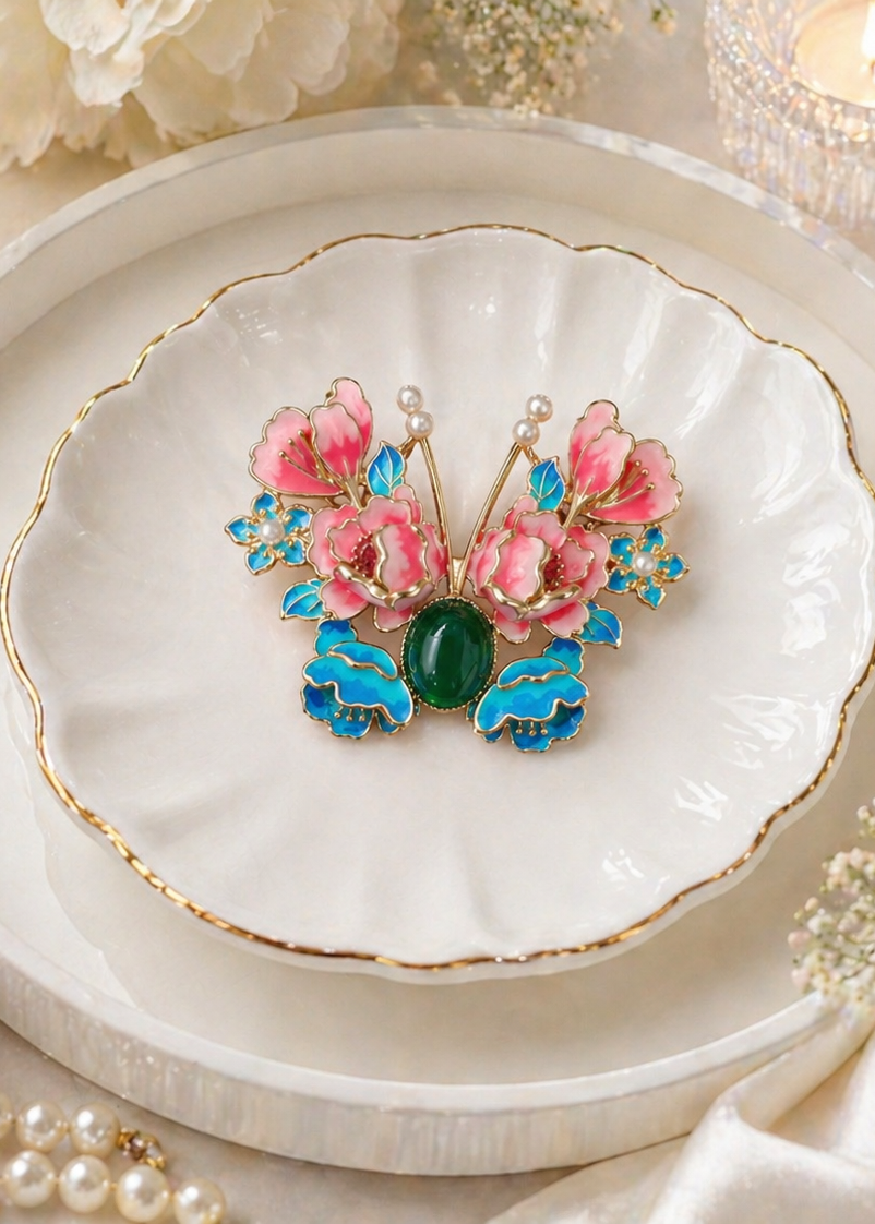 Butterfly-shaped brooch with pink flowers and green stone on a decorative plate