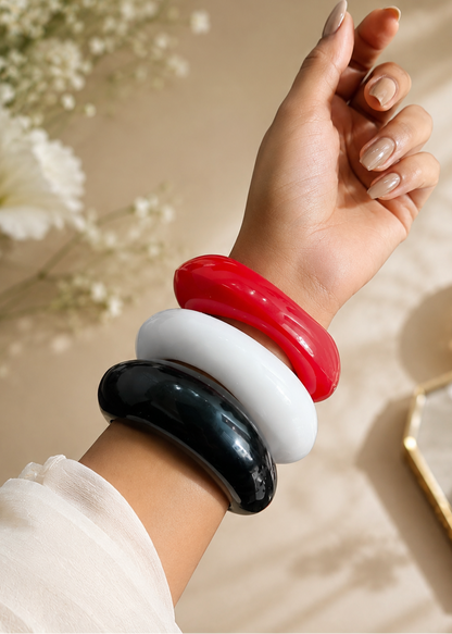 Hand wearing three colorful bangles on a neutral background with flowers.