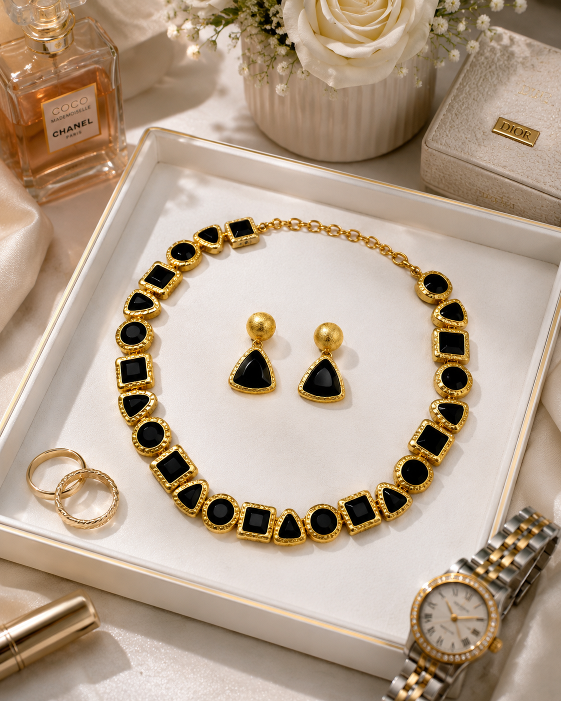 Gold and black jewelry set including necklace and earrings and flowers in the background.