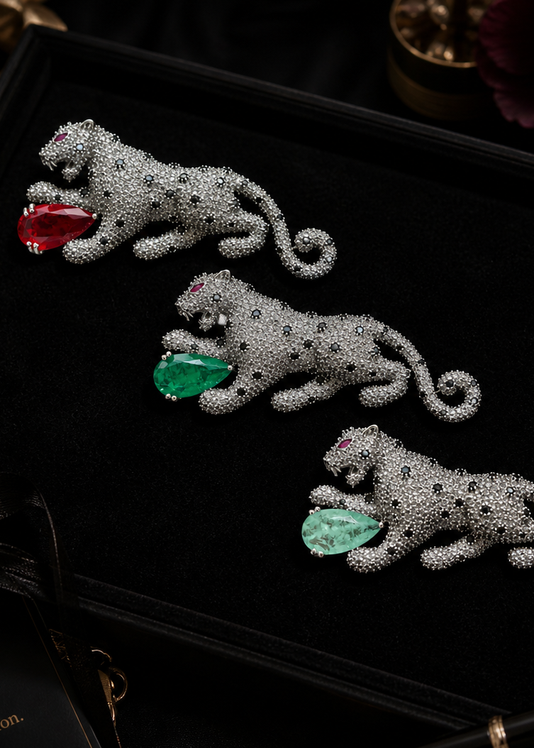 Three silver tiger brooches with gemstones on a black background