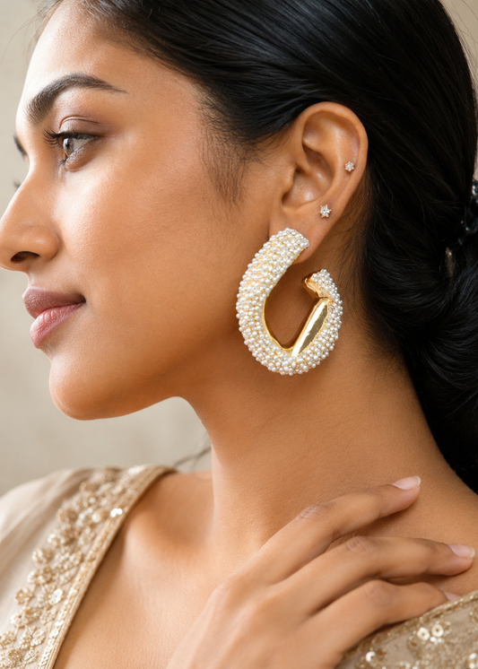 Woman wearing large pearl hoop earrings with a neutral background