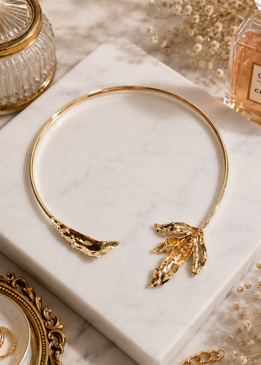 Aurora Gold Leaf Statement Necklace displayed on a marble surface featuring sculpted gold leaf detailing and a polished finish.