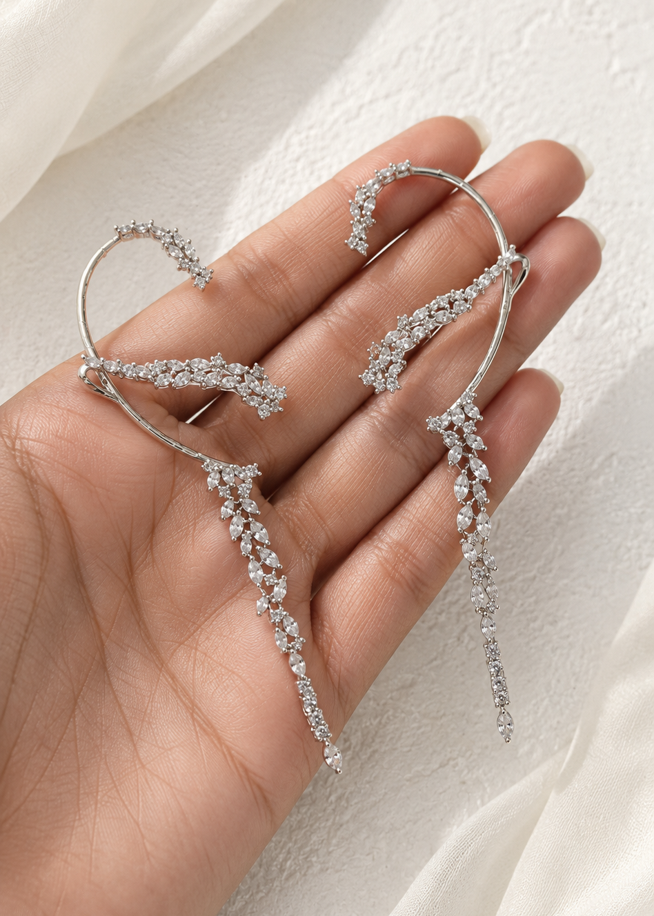 Close-up of Celestia Cascade silver crystal ear cuffs with cascading leaf design held on hand.