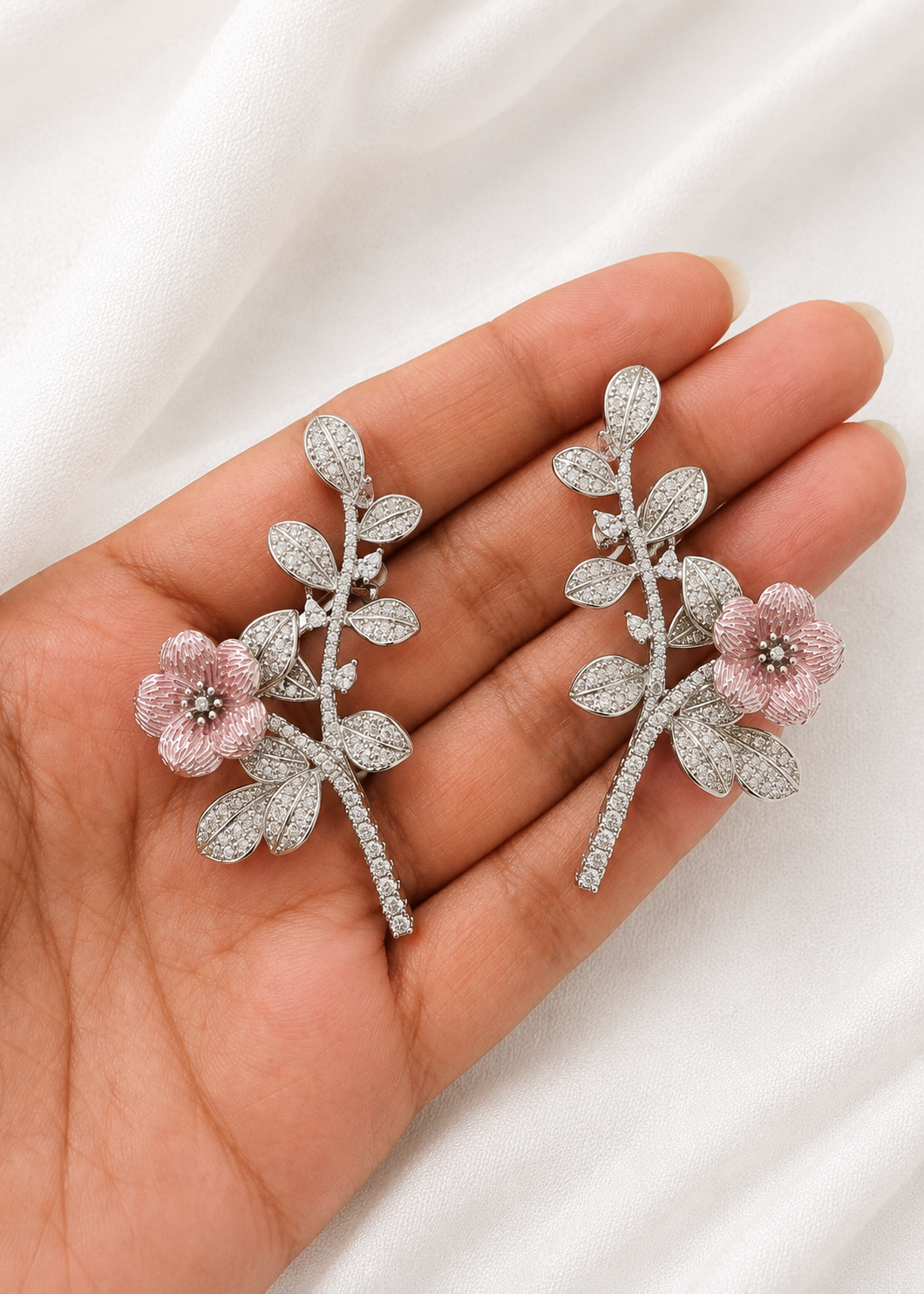 Silver floral ear cuffs with blush pink enamel flower and sparkling cubic zirconia leaves displayed on hand.